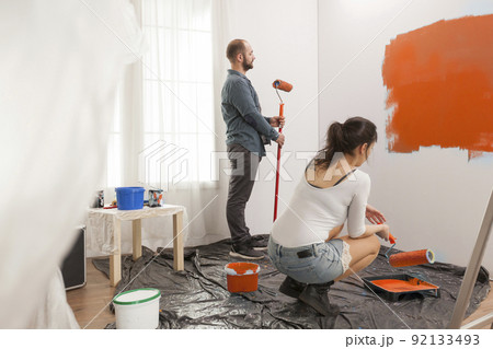 Family painting room with orange color paint to redecorate apartment with paintbrush and roller. Couple doing diy manual renovation using decorating tools and equipment, housework change. 92133493
