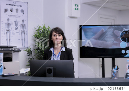 Portrait of smiling front desk receptionist waiting to greet patients in private practice clinic lobby. Professional healthcare worker offering support for hospital appointments. 92133654