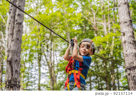 Happy child in a helmet, healthy teenager school boy enjoying activity in a climbing adventure park on a summer day 92137114