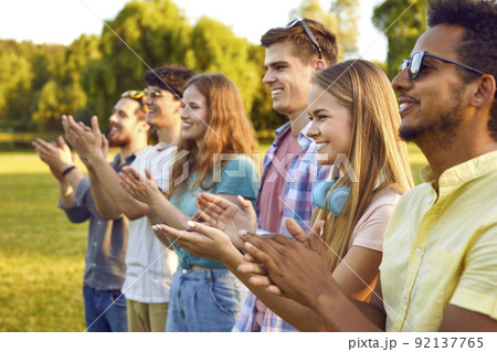 Diverse group of happy young people clapping hands at an outdoor summer festival 92137765
