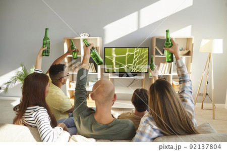 Young people relax at home with beer watching football 92137804