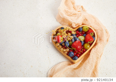 Berries mix in in a heart shaped bowl on travertine background Berries mix in in a heart shaped bowl on travertine background 92140134