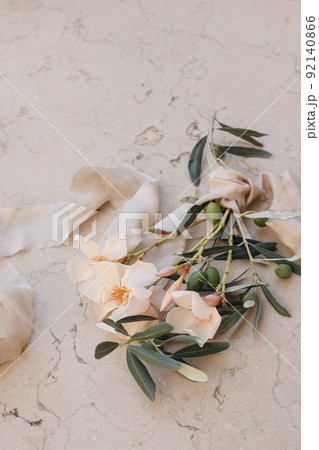 Summer wedding floral composition. Closeup of apricot oleander blossom, flowers and green olive tree branches. Beige marble background with silk ribbon. Blurred background, selective focus. Vertical. Summer wedding floral composition. Closeup of apricot oleander blossom, flowers and green olive tree branches. Beige marble background with silk ribbon. Blurred background, selective focus. Vertical. 92140866