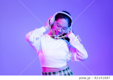 Young asian woman in white shirt wearing headphones posing on blue and purple background.. 92141087