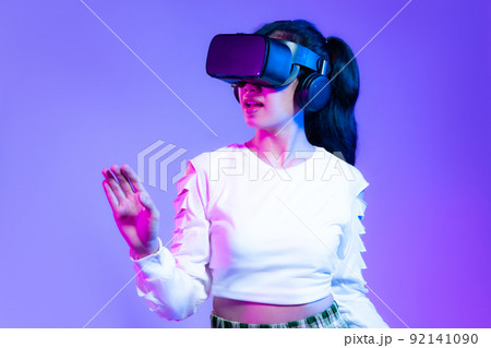 Metaverse concept, young asian girl in white fashion sweatshirt wearing vr headset playing hand touching online game on purple background.. Metaverse concept, young asian girl in white fashion sweatshirt wearing vr headset playing hand touching online game on purple background.. 92141090