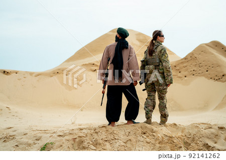 Man with veil stay with military or soldier woman in desert and look around Man with veil stay with military or soldier woman in desert and look around 92141262