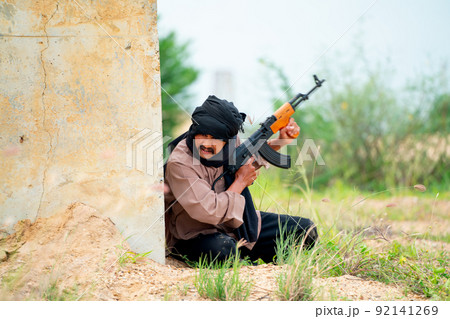 Terrorist with veil stay behind of concrete wall also hold gun to prepare for fight with the enemy Terrorist with veil stay behind of concrete wall also hold gun to prepare for fight with the enemy 92141269
