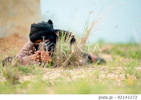 Terrorist with veil lie on the ground and point gun to the enemy in grass field with day light. Terrorist with veil lie on the ground and point gun to the enemy in grass field with day light. 92141272