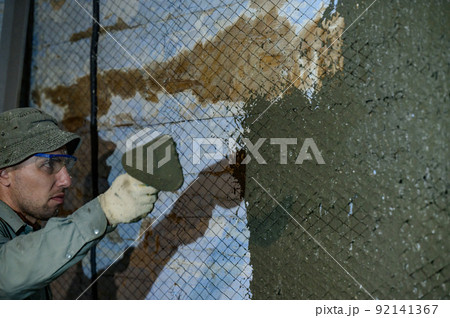The master throws a solution of liquid concrete on the wall, the first layer of plaster on the wall. The master throws a solution of liquid concrete on the wall, the first layer of plaster on the wall. 92141367