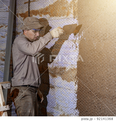 A man throws concrete mortar on the wall, the first layer of plaster on the wall, repair work in Ukraine. A man throws concrete mortar on the wall, the first layer of plaster on the wall, repair work in Ukraine. 92141368