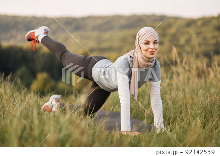 Smiling young woman in hijab and sport outfit doing flexible exercises on yoga mat Smiling young woman in hijab and sport outfit doing flexible exercises on yoga mat 92142539