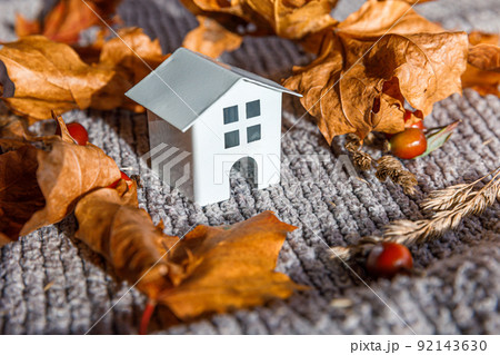 Autumnal Background. Toy house and dried orange fall maple leaves on grey knitted sweater. Thanksgiving banner copy space. Hygge mood cold weather concept. Hello Autumn with family. 92143630