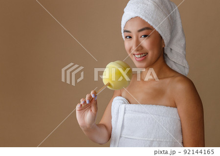 Cheerful Asian woman holding lollipop bath sponge Cheerful Asian woman holding lollipop bath sponge 92144165