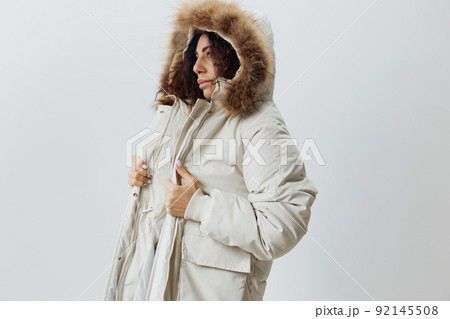 Serious Curly Pretty Latin Lady Wearing Fur Hood Of Soft Warm Beige Winter Coat Posing Isolated Looking Aside At White Studio Background. Fashion Huge Sale New Collection Concept Vertical Side Shot Serious Curly Pretty Latin Lady Wearing Fur Hood Of Soft Warm Beige Winter Coat Posing Isolated Looking Aside At White Studio Background. Fashion Huge Sale New Collection Concept Vertical Side Shot 92145508