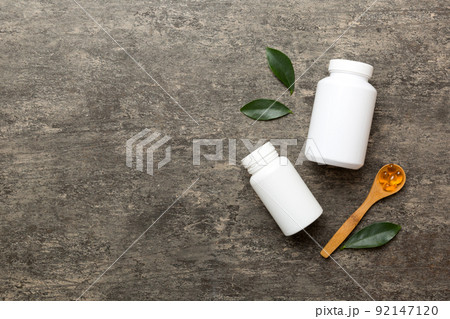 Omega-3 capsules lie in white bottle on a table with green leaves background. Fish oil tablets. Biologically active additives. omega 6, omega 9, vitamin A, E, D, vitamin D3 top view with copy space 92147120