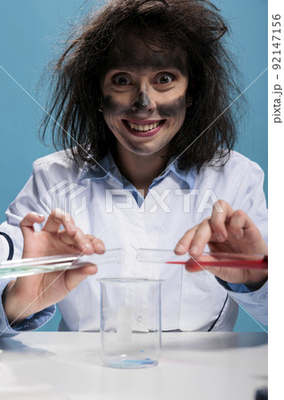 Crazy foolish biochemist with beakers experimenting new formula discovered by mistake in laboratory explosion. Insane maniac chemist mixing toxic unidentified compounds using glass tubes and beaker Crazy foolish biochemist with beakers experimenting new formula discovered by mistake in laboratory explosion. Insane maniac chemist mixing toxic unidentified compounds using glass tubes and beaker 92147156