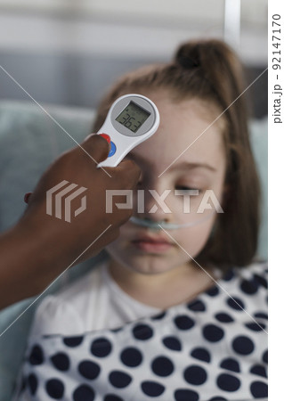 Close up shot of pediatric hospital nurse measuring sick little girl body temperature using thermometer. Children healthcare clinic medical staff examining illness evolution of ill kid under treatment 92147170