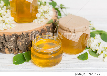 Sweet honey jar surrounded spring acacia blossoms. Honey flows from a spoon in a jar. jars of clear fresh acacia honey on wooden background 92147760