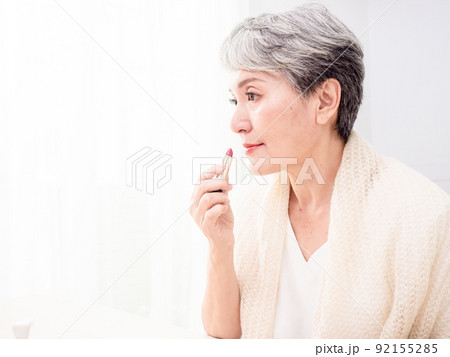 Portrait of mature aged asian woman 60s applying lipstick looking at mirror. Portrait of mature aged asian woman 60s applying lipstick looking at mirror. 92155285