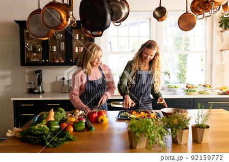 Image of happy caucasian mother and adult daughter preparing meal in kitchen Image of happy caucasian mother and adult daughter preparing meal in kitchen 92159772