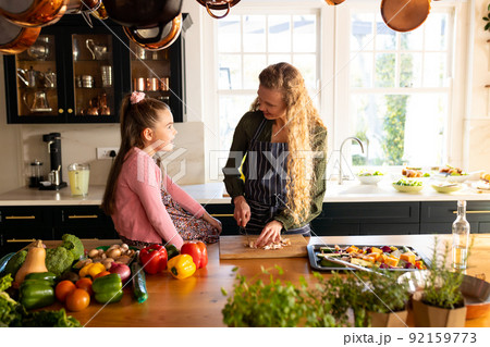 Image of happy caucasian mother and daughter preparing meal in kitchen 92159773