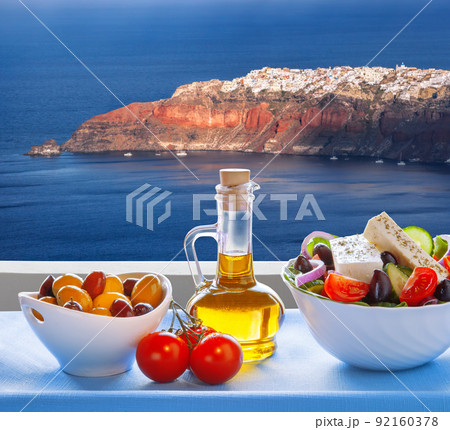 Greek salad against famous Oia village, Santorini island in Greece Greek salad against famous Oia village, Santorini island in Greece 92160378