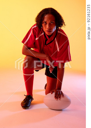 Portrait of african american female rugby player with rugby ball over neon yellow lighting 92161235