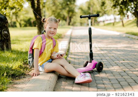A pretty girl is resting on the way from school, playing on the phone or texting friends.. Modern technology, back to school A pretty girl is resting on the way from school, playing on the phone or texting friends.. Modern technology, back to school 92162343