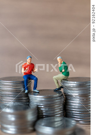 Miniature people A businessman is seated atop a mound of money 92162404