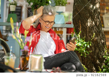 A woman in red shirt sitting outside and spending time online 92162569