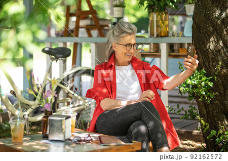 A woman in red shirt sitting outside and spending time online 92162572