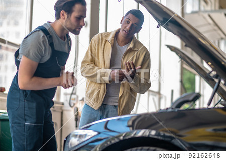 Customer looking questioningly at mechanic near hood of car Customer looking questioningly at mechanic near hood of car 92162648