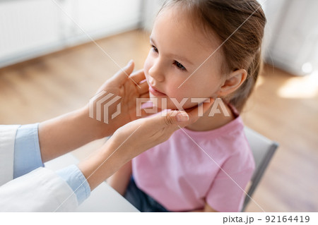 doctor checking girl patient's tonsils at clinic 92164419