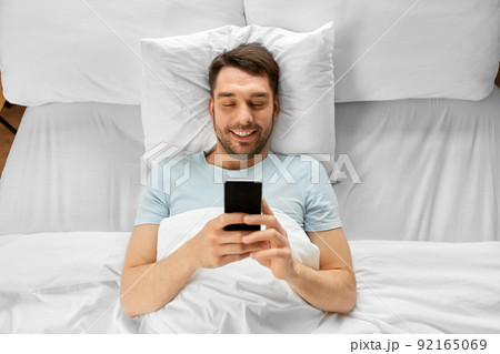 man with smartphone in bed in morning at home man with smartphone in bed in morning at home 92165069