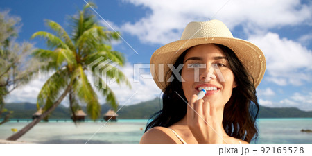 smiling woman in bikini with lip balm on beach 92165528