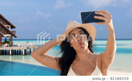 smiling woman in bikini taking selfie on beach 92166350