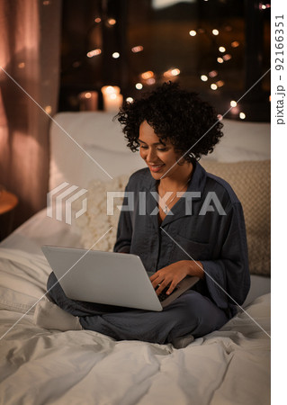 happy woman with laptop sitting in bed at night 92166351