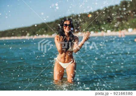 woman in bikini splashing sea water on beach 92166380