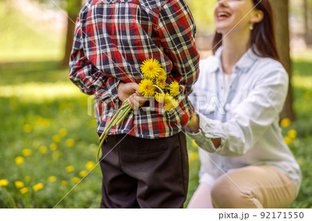 Close up of dandelions in small boy hand behind back before giving to mother. Flowers for mom. Close up of dandelions in small boy hand behind back before giving to mother. Flowers for mom. 92171550