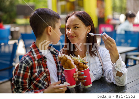 Beautiful young mother and small cute son eating waffles in city on summer day. Weekend. 92171552