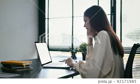 Focused female employee using laptop, working on research project at bright modern office 92171985