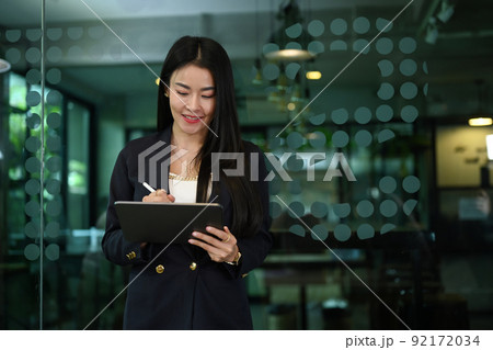 Asian woman manager writing some information on document while standing in corporate office 92172034