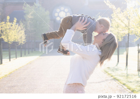 a young and happy mother and child, playing, stands in the middle of a park in the rays of the 92172516