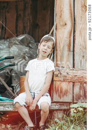 a tired boy sits leaning against the barn door with his eyes closed. child labor in the countryside a tired boy sits leaning against the barn door with his eyes closed. child labor in the countryside 92173068