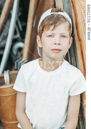 portrait of a tired boy sits leaning against the barn door with green eyes. Child labor in the countryside 92173069