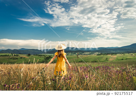 Woman in yellow dress and hat staying at the green meadow in the mountain Woman in yellow dress and hat staying at the green meadow in the mountain 92175517