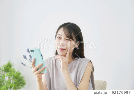 リビングでスマホを持って想像する女性 92176997
