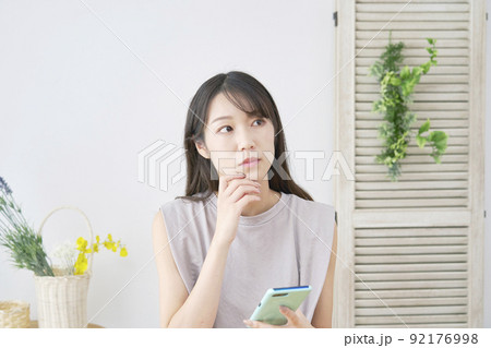 リビングでスマホを持って考える女性 リビングでスマホを持って考える女性 92176998