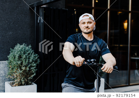 Pleasant smiling man riding a kick scooter Pleasant smiling man riding a kick scooter 92179154