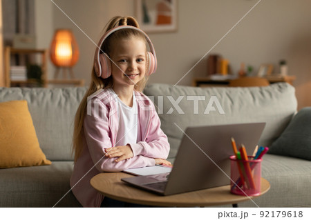 Cute Schoolgirl Using Laptop Wearing Pink Headphones Sitting At Home 92179618